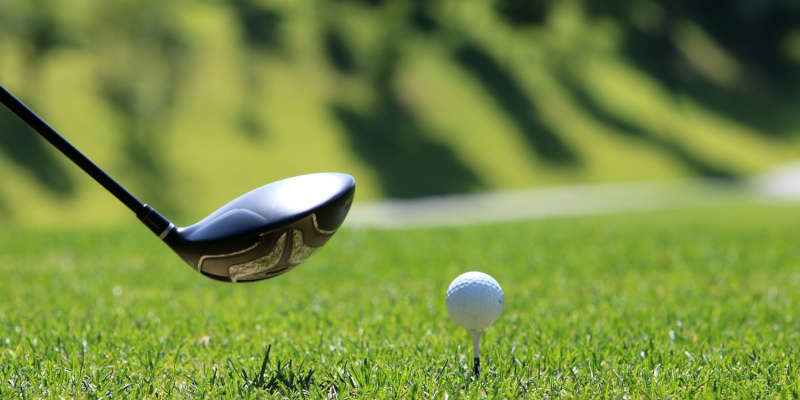 A golf stick preparing to hit a golf ball.